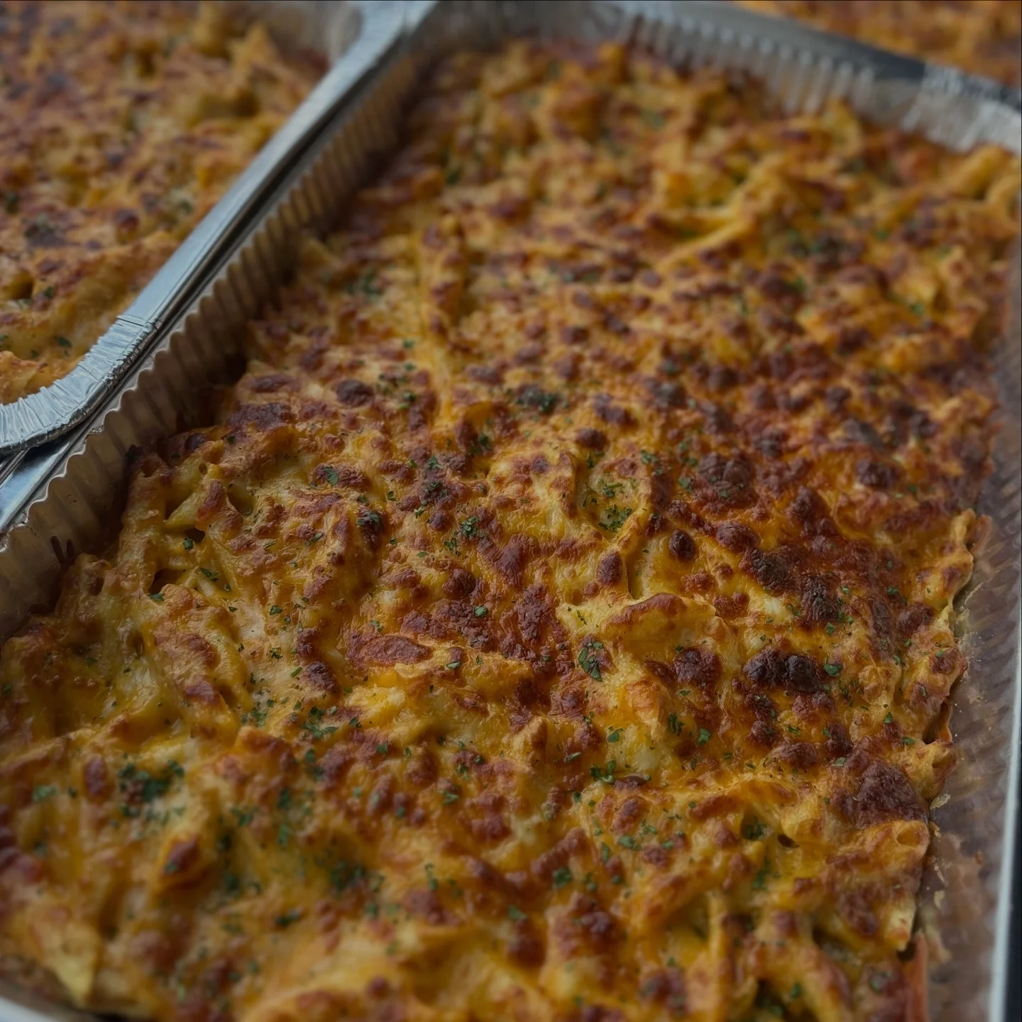 A baked pasta dish with a golden-brown, cheesy crust, showing a blend of ingredients baked to perfection in a silver tray.