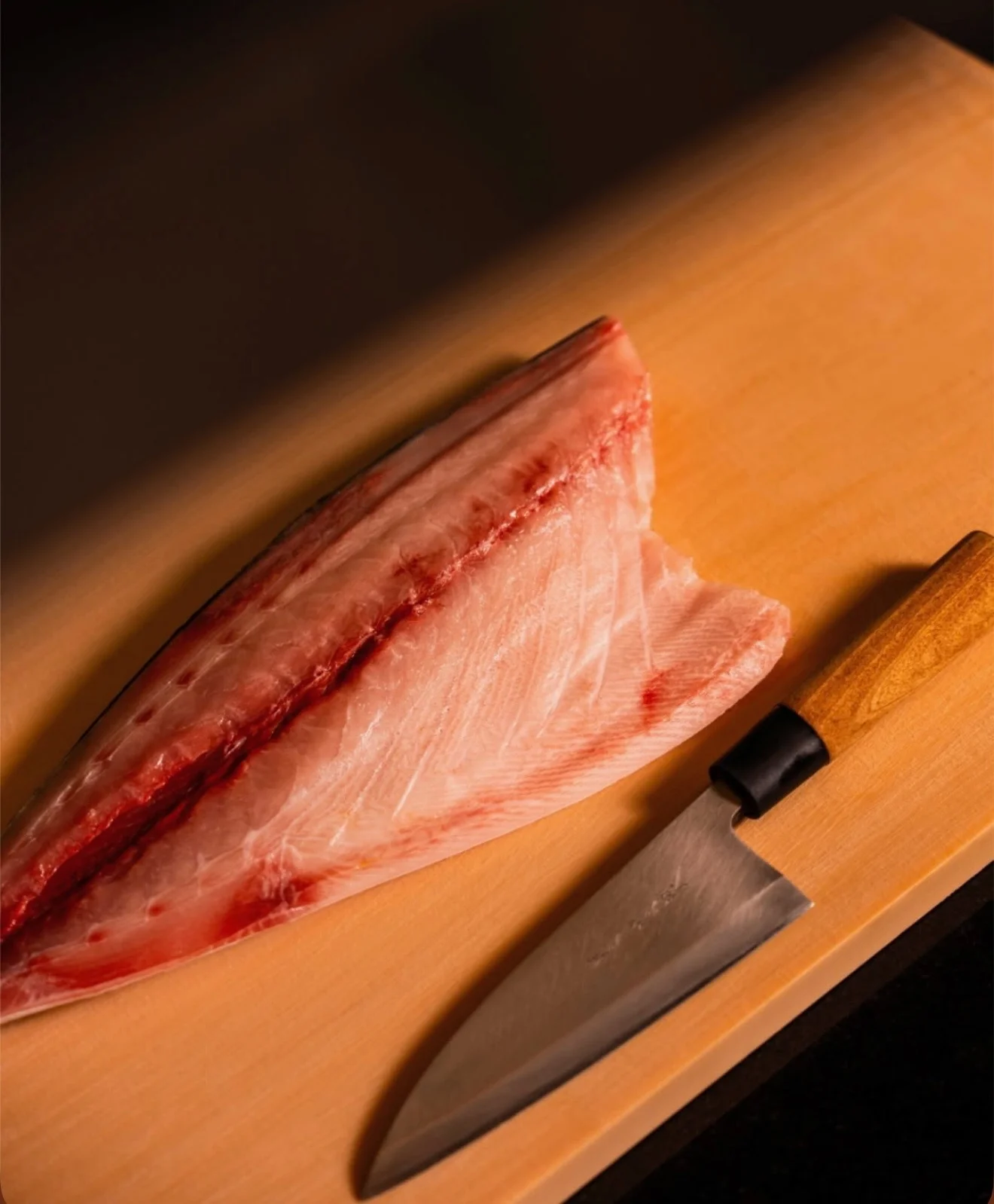 Fresh fish fillet and a sharp knife on a wooden cutting board.