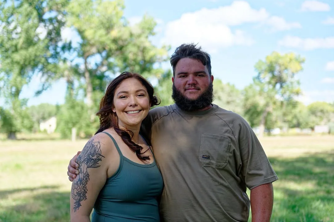 A smiling couple posing together outdoors in a grassy field, embodying a relaxed and friendly atmosphere.