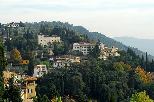 A picturesque hillside village with houses surrounded by trees and scenic mountains in the background.