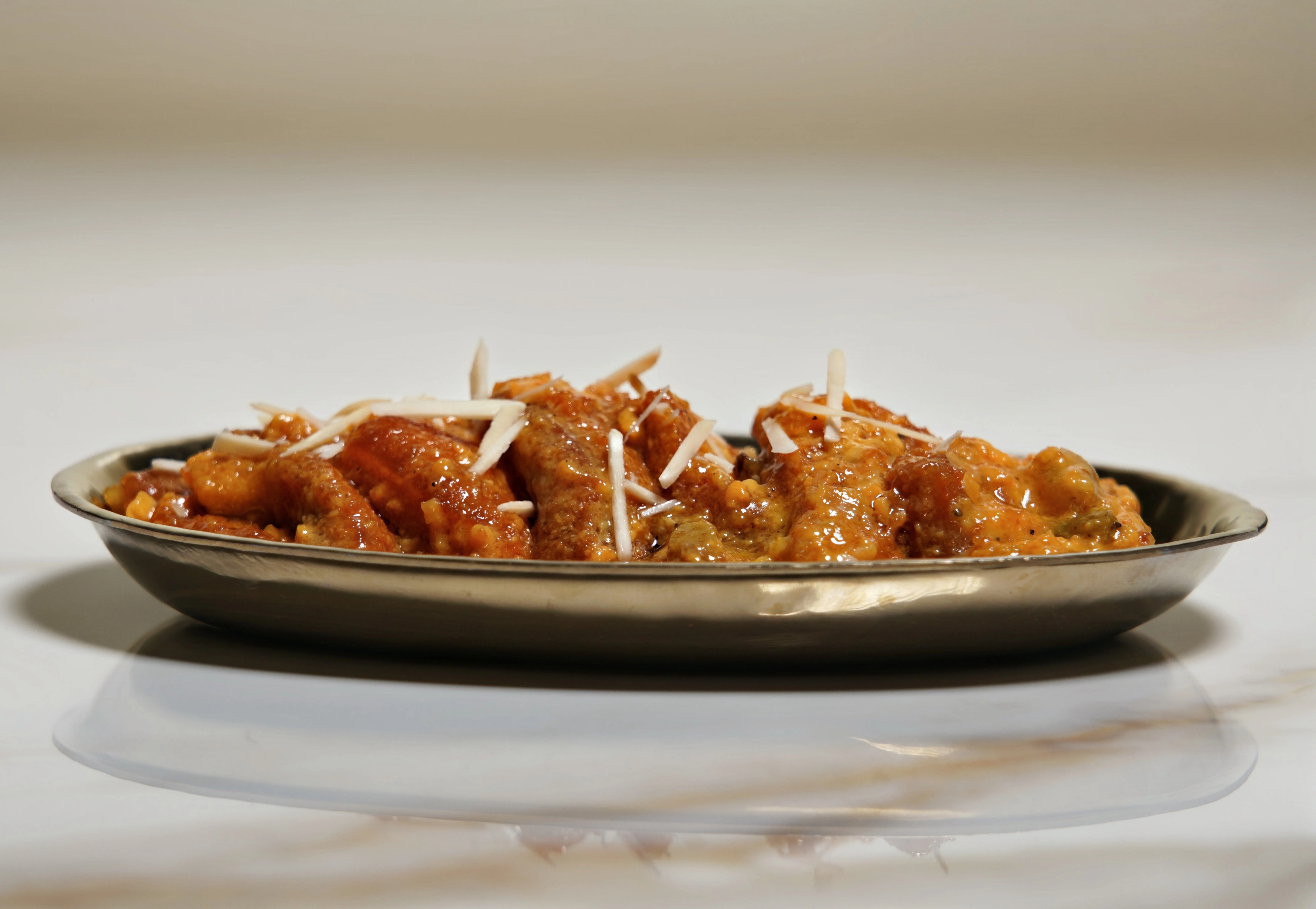 A silver plate filled with a sweet dish topped with slivers of almonds. The dish has a rich, sticky sauce coating the pieces.