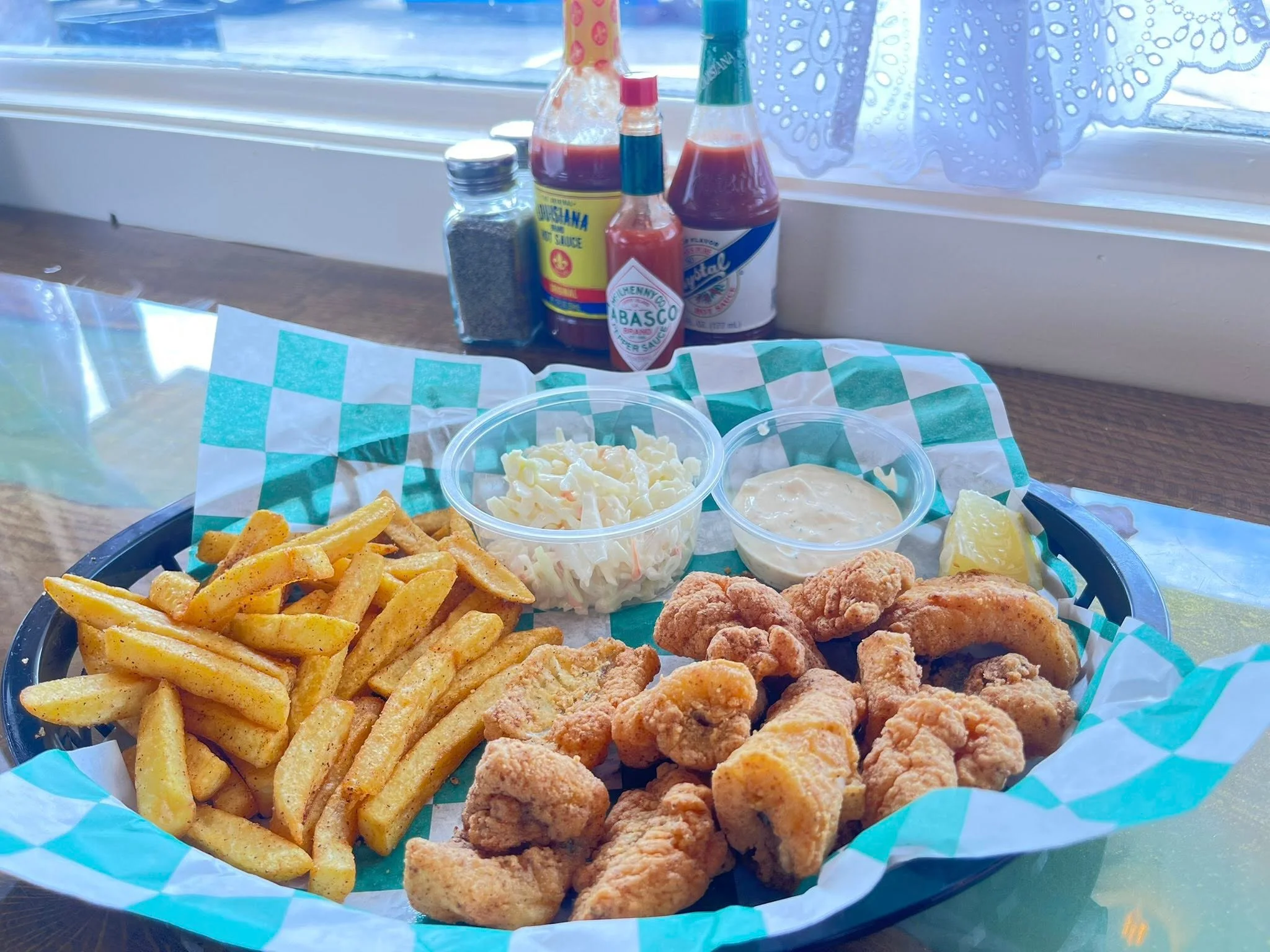 Fried seafood platter with fries, coleslaw, and sauces on a checkered tray.