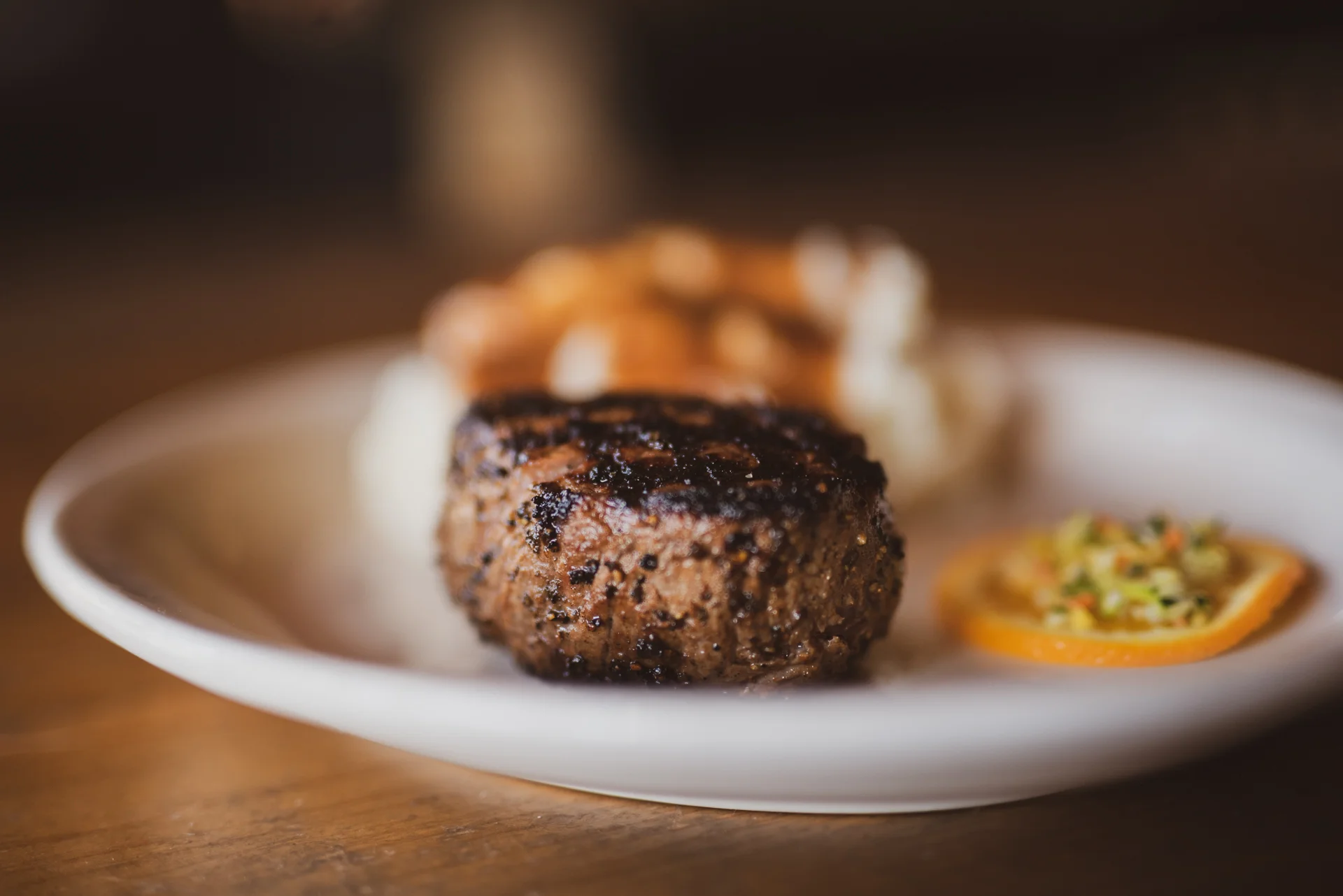 Grilled beef patty served with mashed potatoes and a citrus garnish.