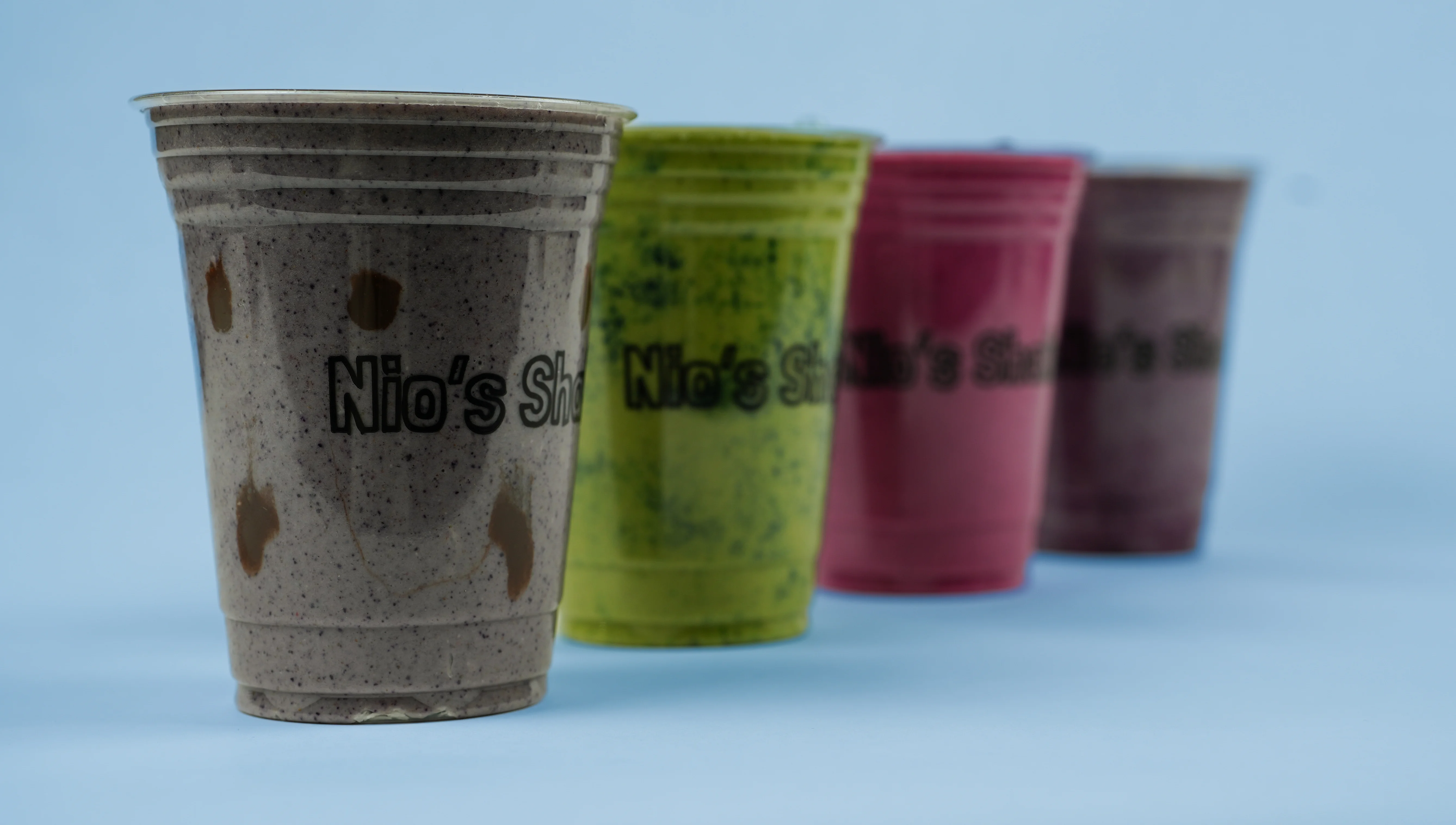 Four colorful milkshakes in tall glasses with whipped cream and toppings.