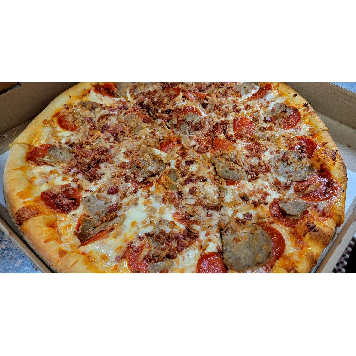 A large pizza topped with pepperoni, sausage, and crispy bacon bits. The cheese is bubbling and slightly browned.