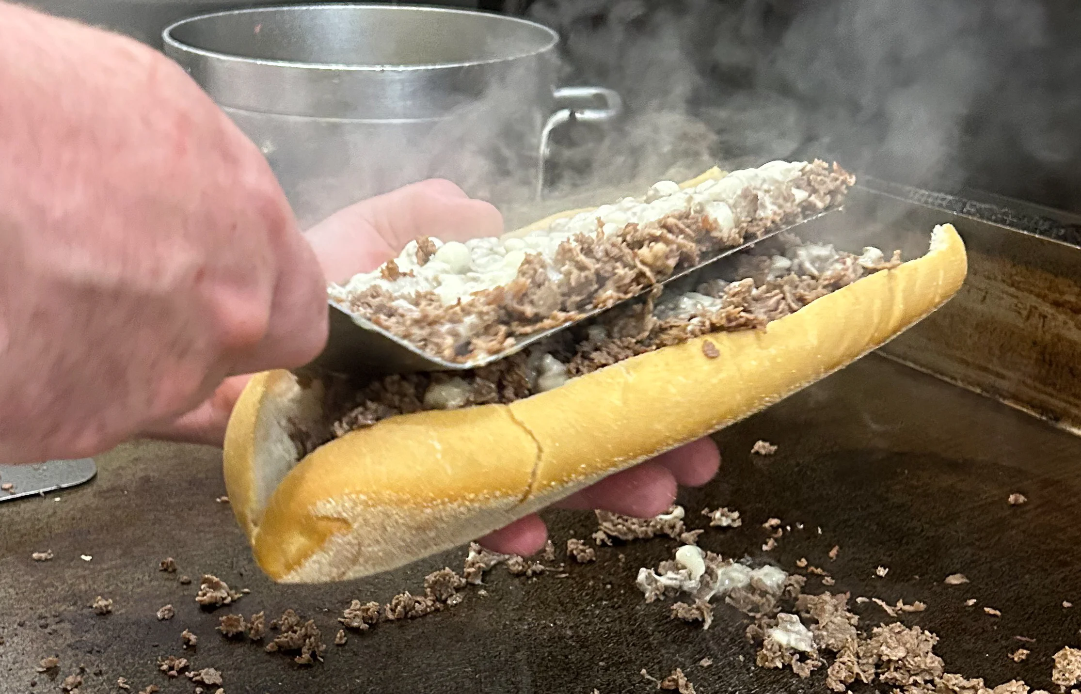 Steak Out cheesesteak being prepared on the grill, with fresh chopped steak filling a toasted hoagie roll.
