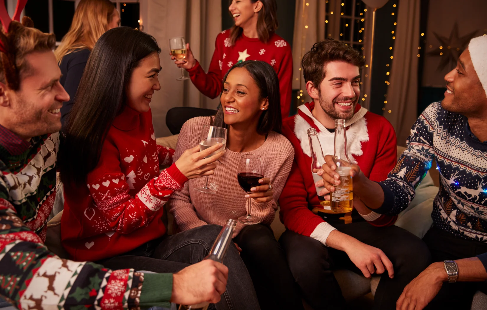 Group of friends celebrating with drinks in festive sweaters