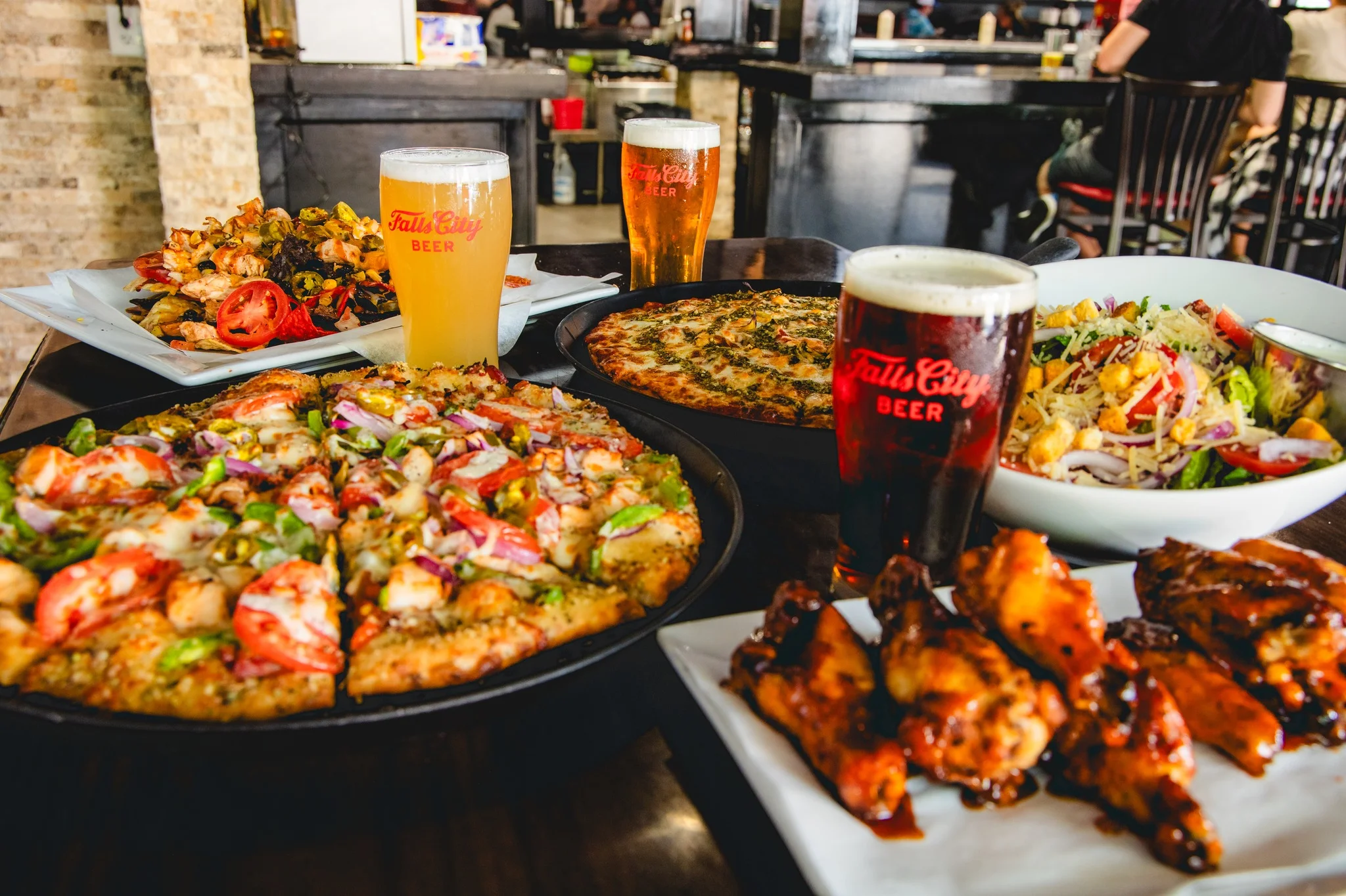 Assorted pizzas and wings with craft beers in a lively restaurant setting
