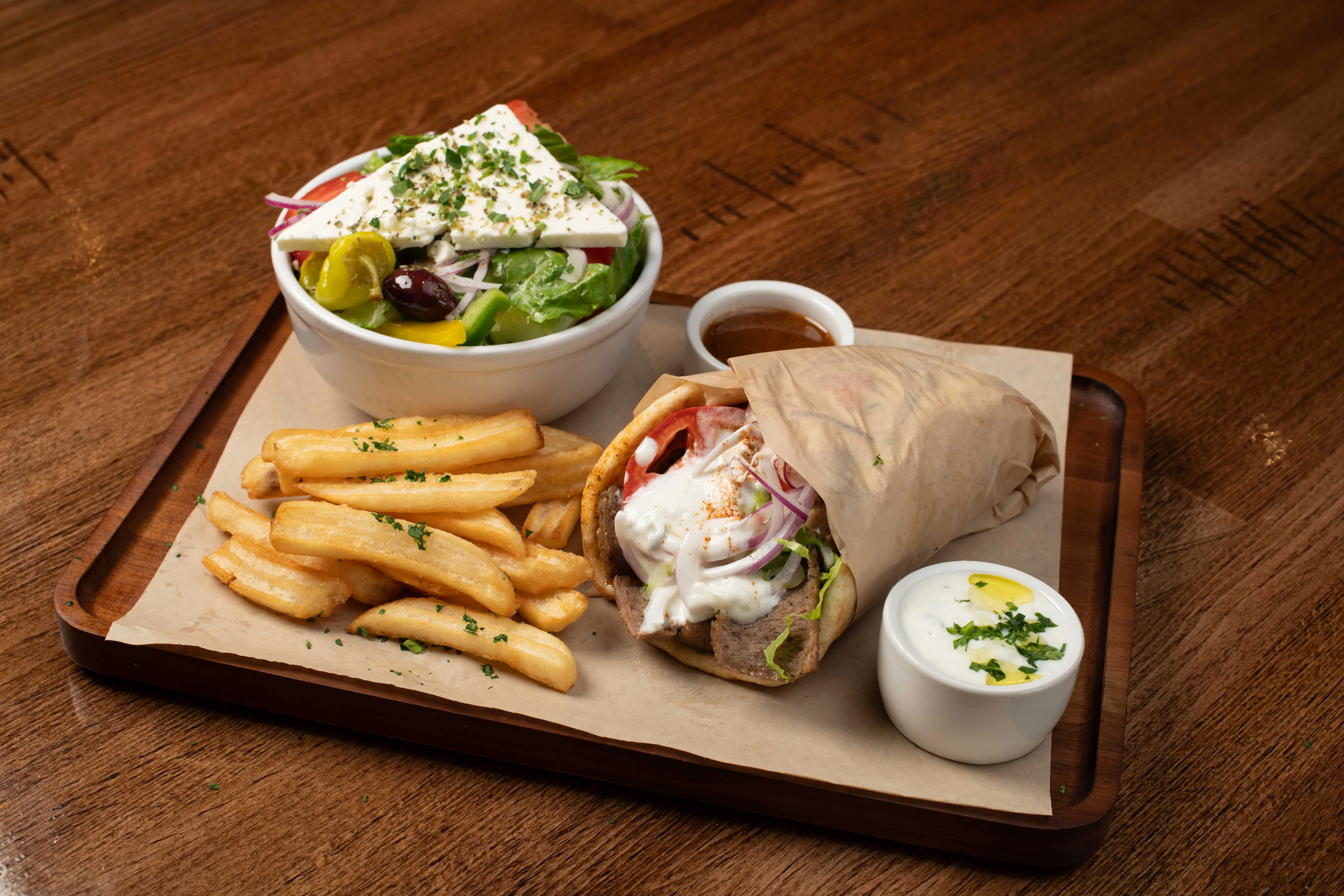 Greek gyro wrap with salad and fries on a wooden tray