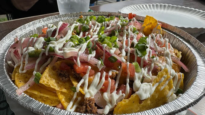 A bowl of nachos topped with ground beef, diced tomatoes, onions, jalapeños, and a drizzle of white sauce.