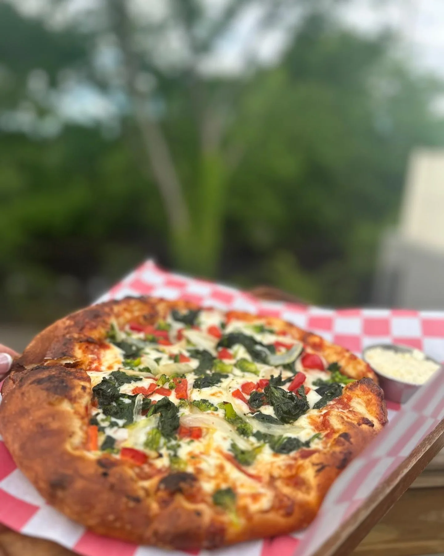 A delicious pizza topped with a variety of vegetables including spinach, red peppers, and onions, served on a checkered platter.