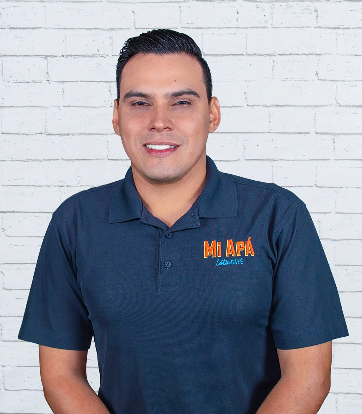 Restaurant team member portrait in branded polo against a white brick wall