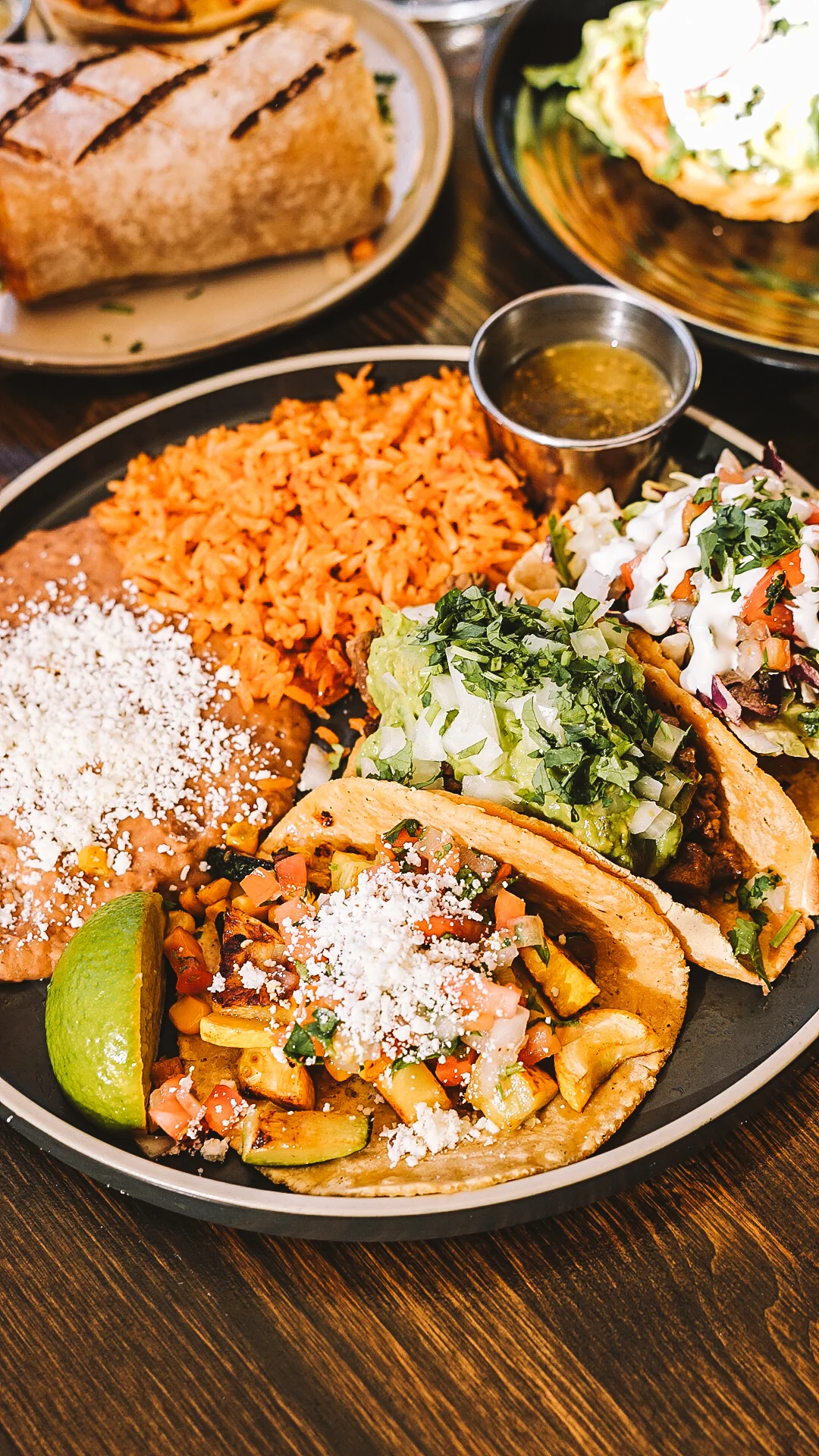 A taco topped with fish, salsa, and garnishes, accompanied by a bowl of sauce on a black plate.