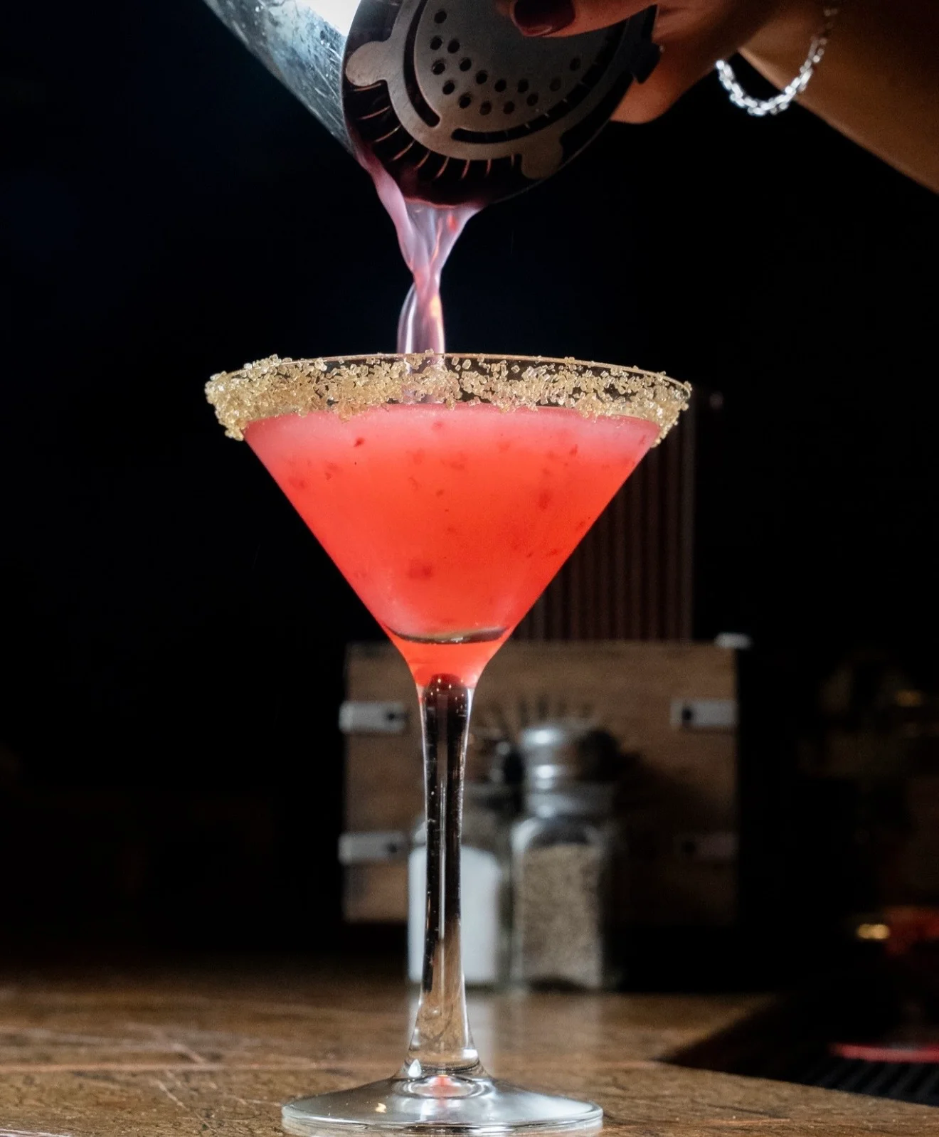 A vibrant cocktail being poured from a shaker into a glass with a sparkling rim.