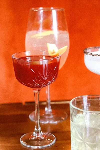 Three colorful cocktails on a wooden table with an orange background.