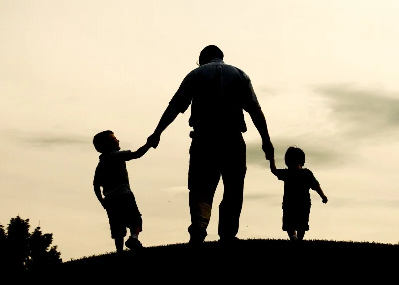 Silhouette of a man holding hands with two children at sunset.
