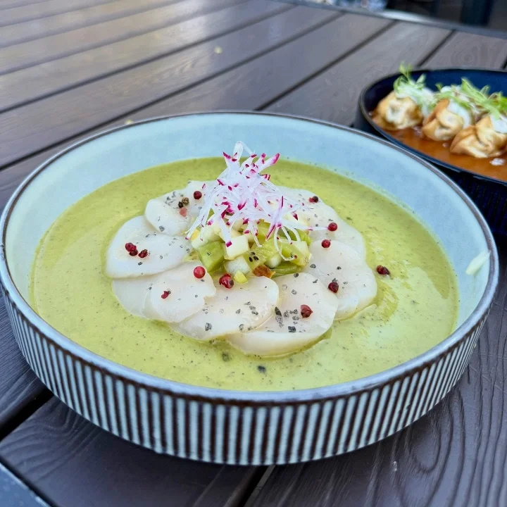 A refined bowl of creamy green sauce topped with scallops, diced vegetables, and pink radish, beautifully presented in a deep dish.