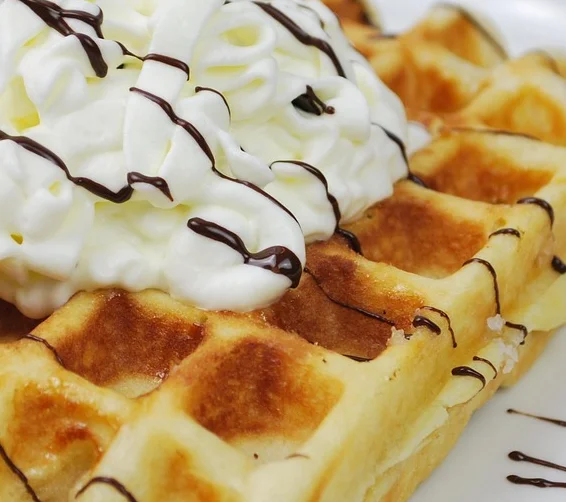 Belgian waffle topped with whipped cream and chocolate drizzle