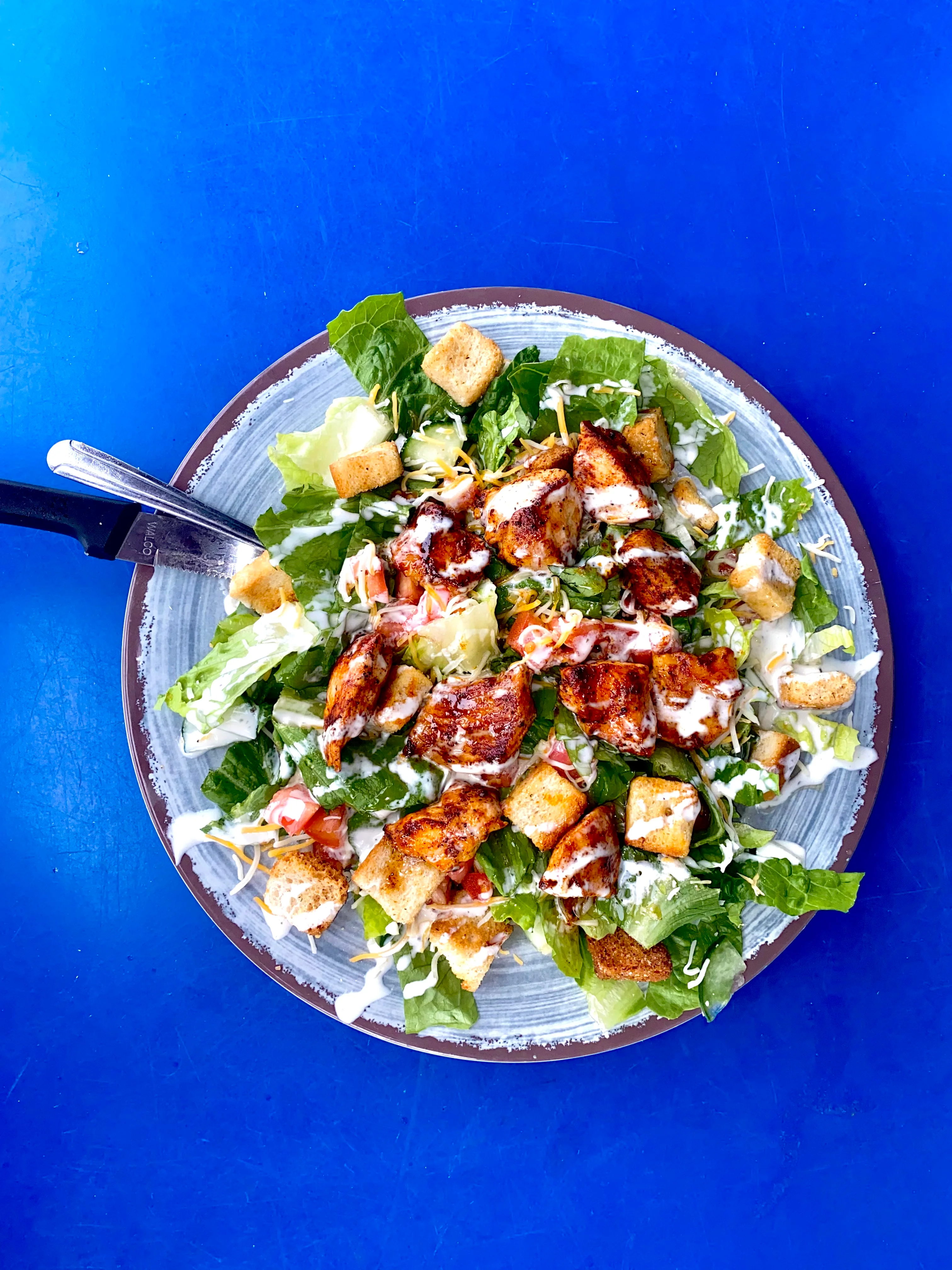 A fresh salad featuring lettuce, croutons, grilled chicken pieces, diced tomatoes, and drizzled dressing, served on a plate.