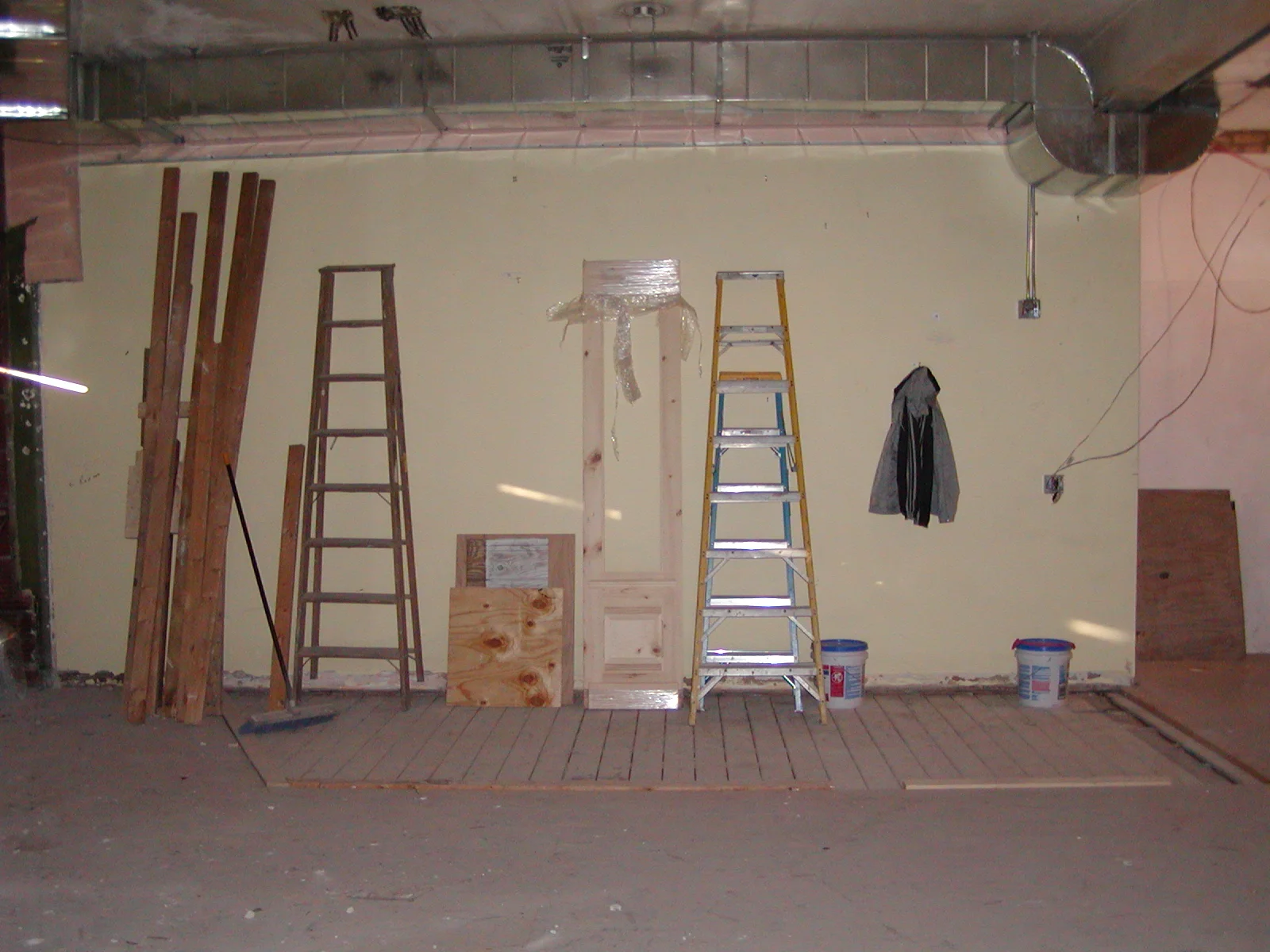 Construction site with ladders and wooden materials against a yellow wall