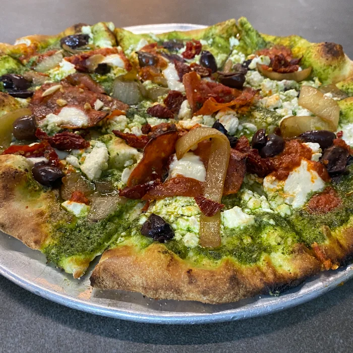 Pesto pizza topped with olives and sun-dried tomatoes