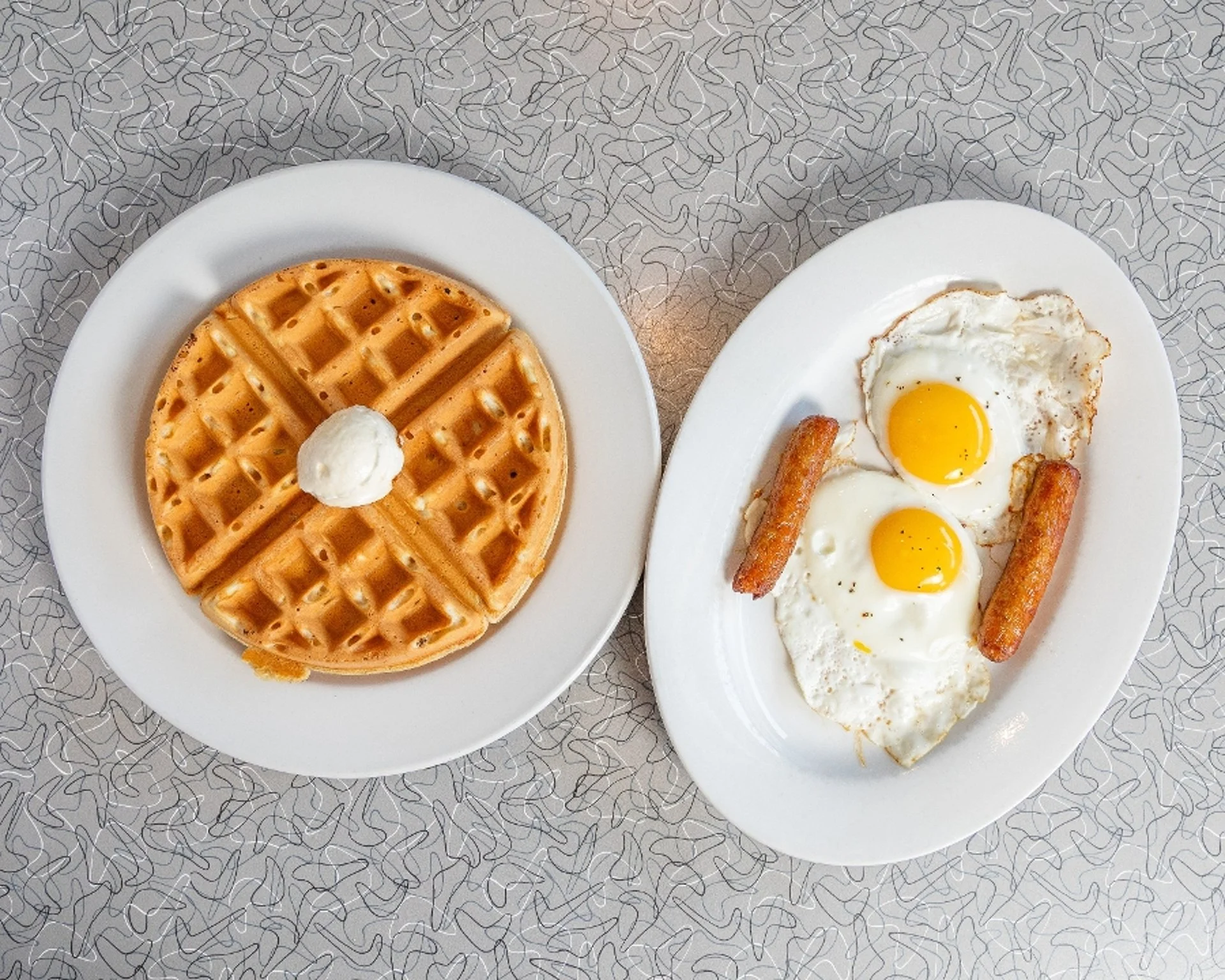 Belgian waffle served with sunny-side-up eggs and breakfast sausage.