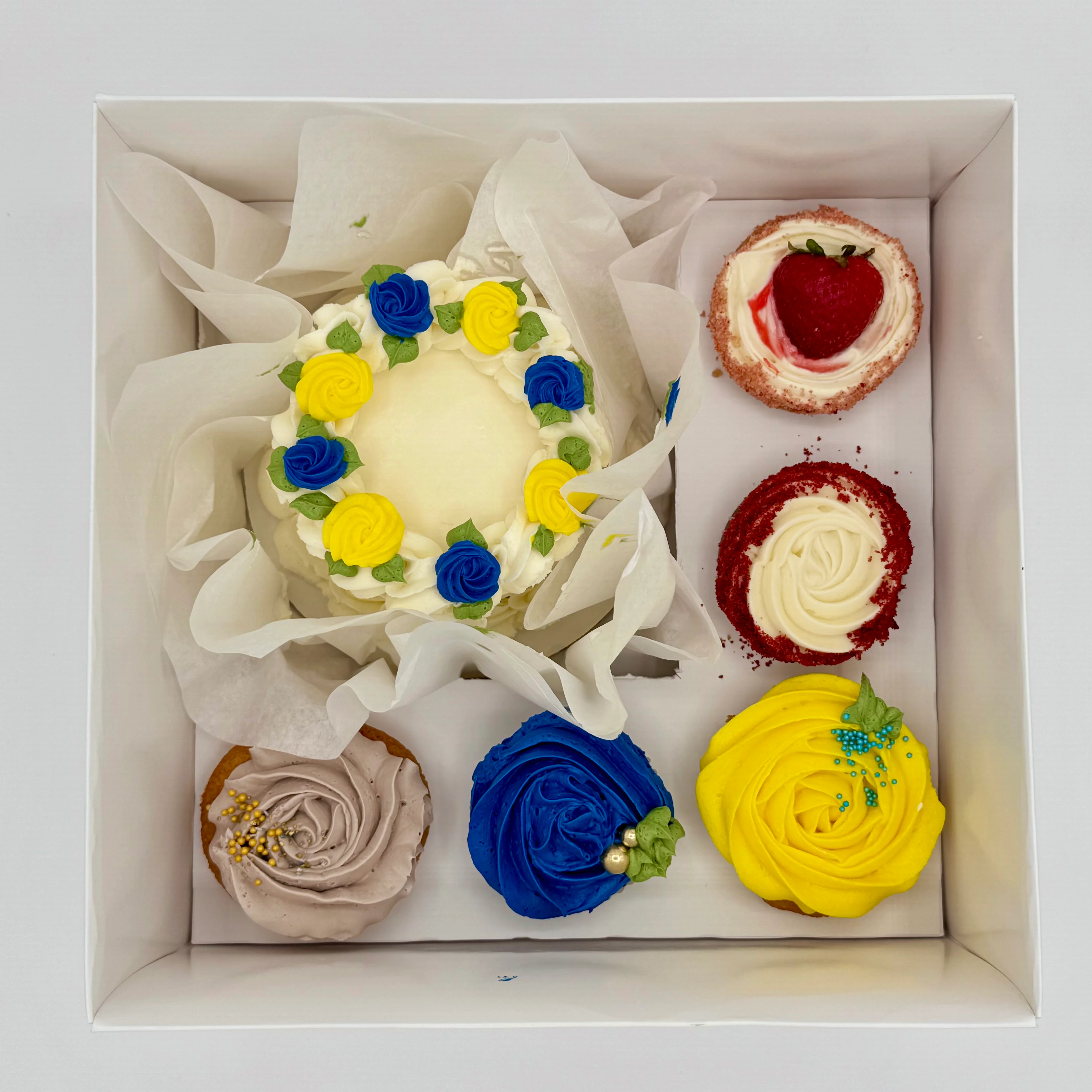 Colorful assortment of decorated cupcakes and cake in a gift box