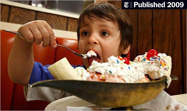 A child enjoys a large serving of ice cream with whipped cream, bananas, and sprinkles in a diner.