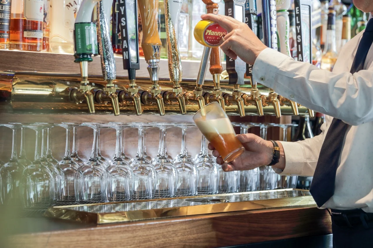 A bartender pouring a beer into a glass with a frothy head.