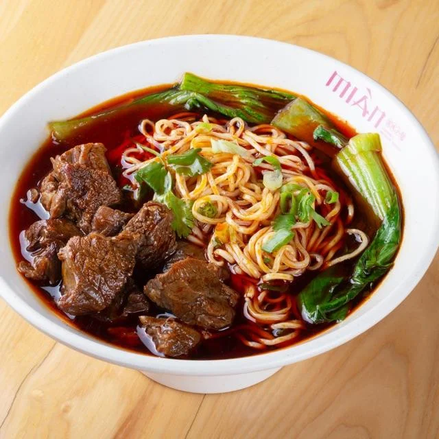 Bowl of spicy braised beef noodles garnished with herbs and spices
