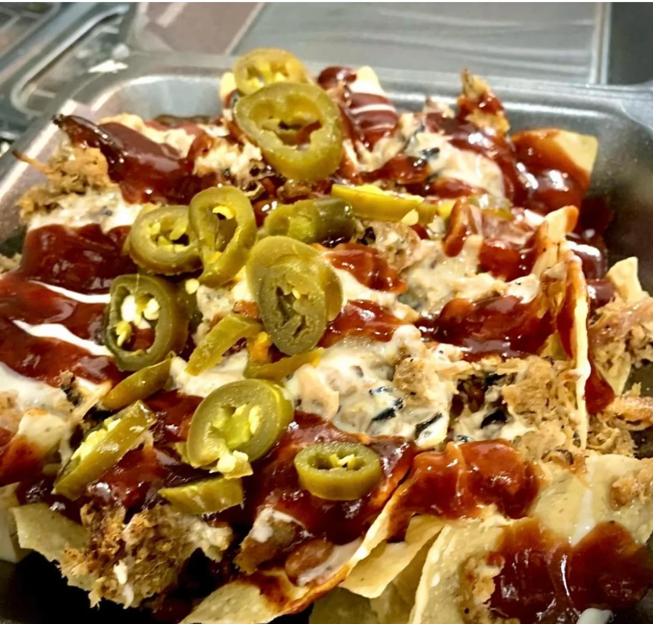 A platter of nachos topped with shredded meat, jalapeños, and drizzled with barbecue sauce.