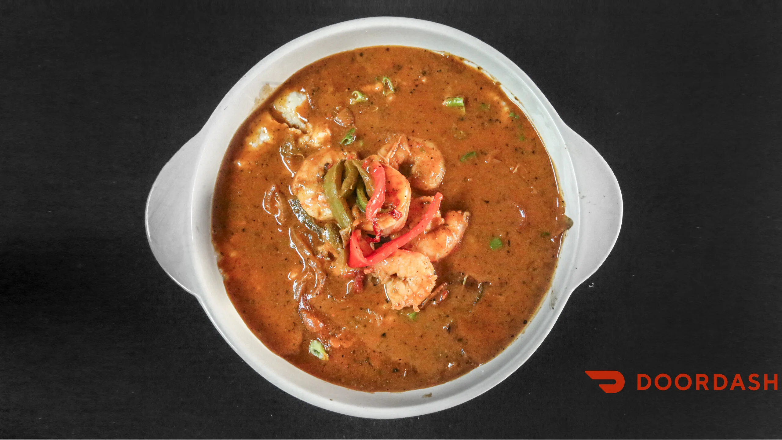 A bowl of spicy shrimp stew with thick sauce, topped with sliced peppers and green onions.