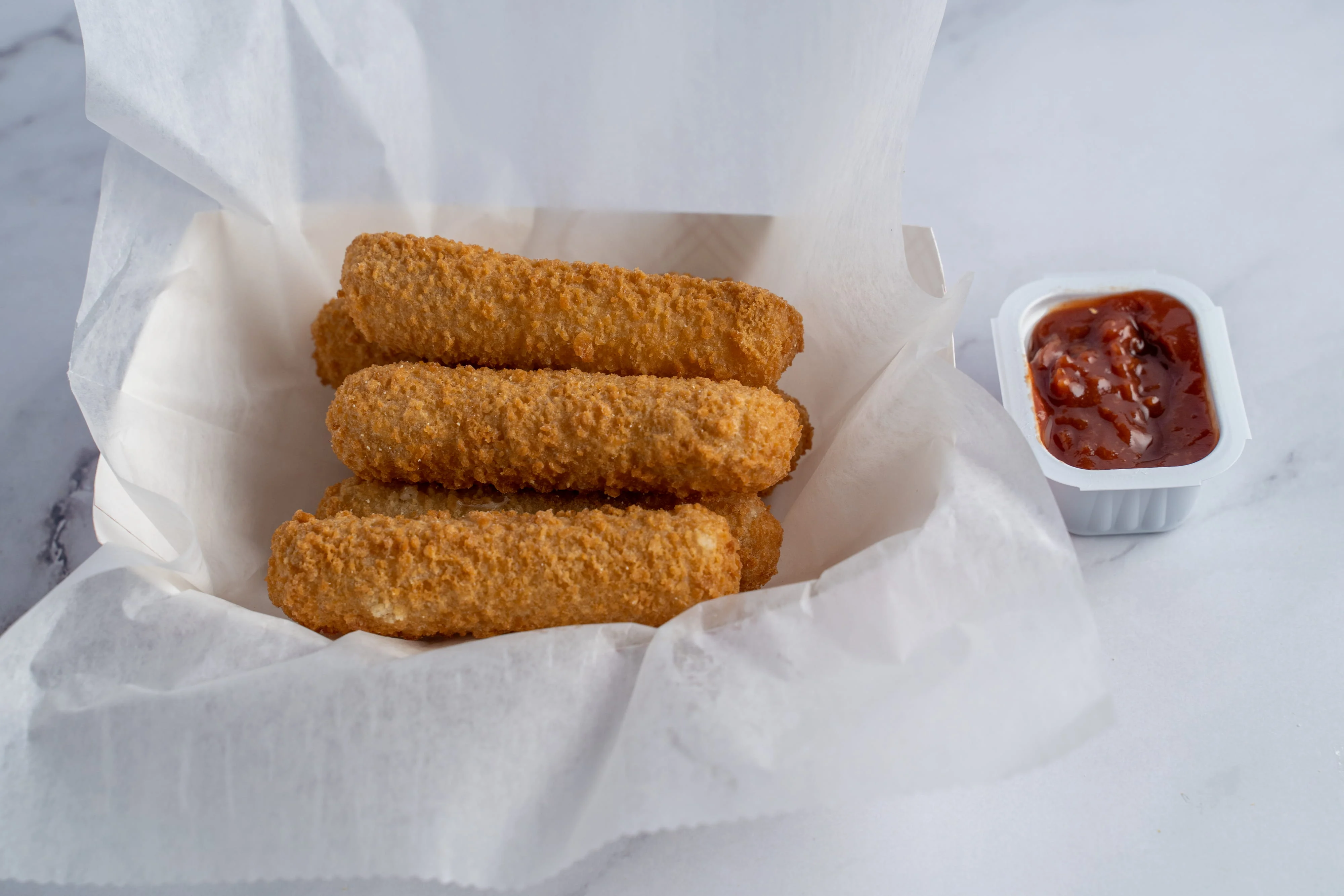 Three crispy breaded cheese sticks with marinara sauce on the side.