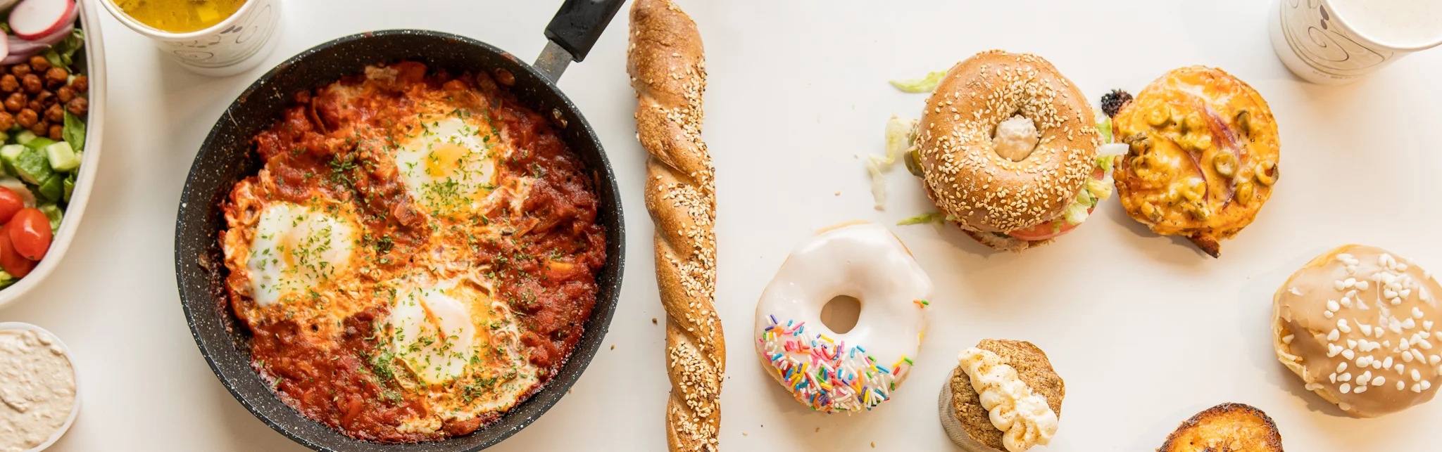 Shakshuka served in a skillet with fresh bread and assorted bagels