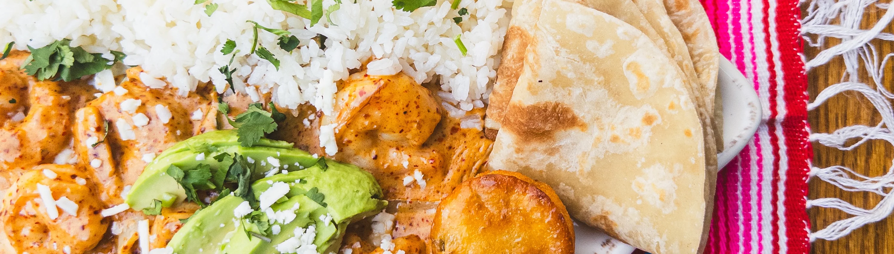 Shrimp enchiladas with rice and black beans on a colorful woven tablecloth