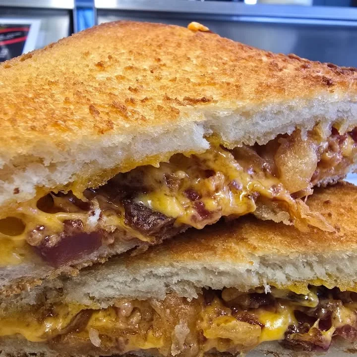 A close-up of a grilled cheese sandwich, revealing melted cheddar cheese and a crunchy golden-brown crust. It showcases the delicious gooeyness inside.