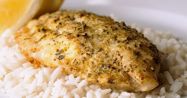 Baked fish fillet served over rice with lemon wedges