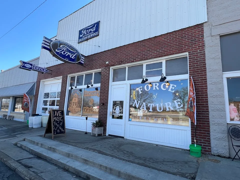 Facade of a building with signs for Ford and a brewery called Force of Nature. The entrance features large windows showcasing brewery branding.