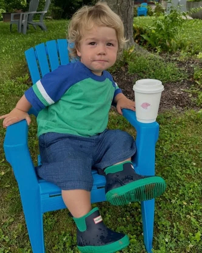 Child sitting in a blue chair with a coffee cup outdoors