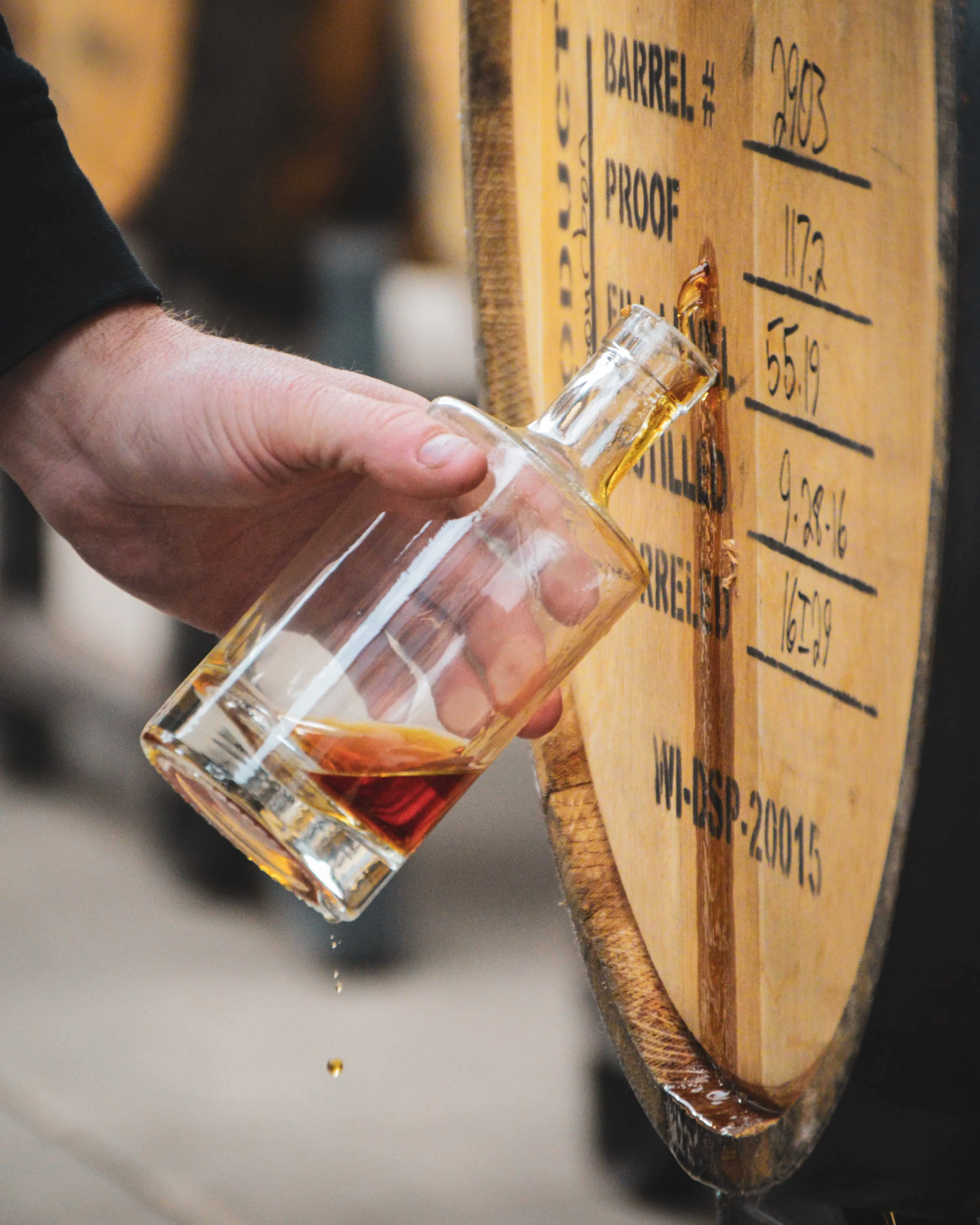 A drop of bourbon falls from a glass as a sample is taken from a whiskey barrel
