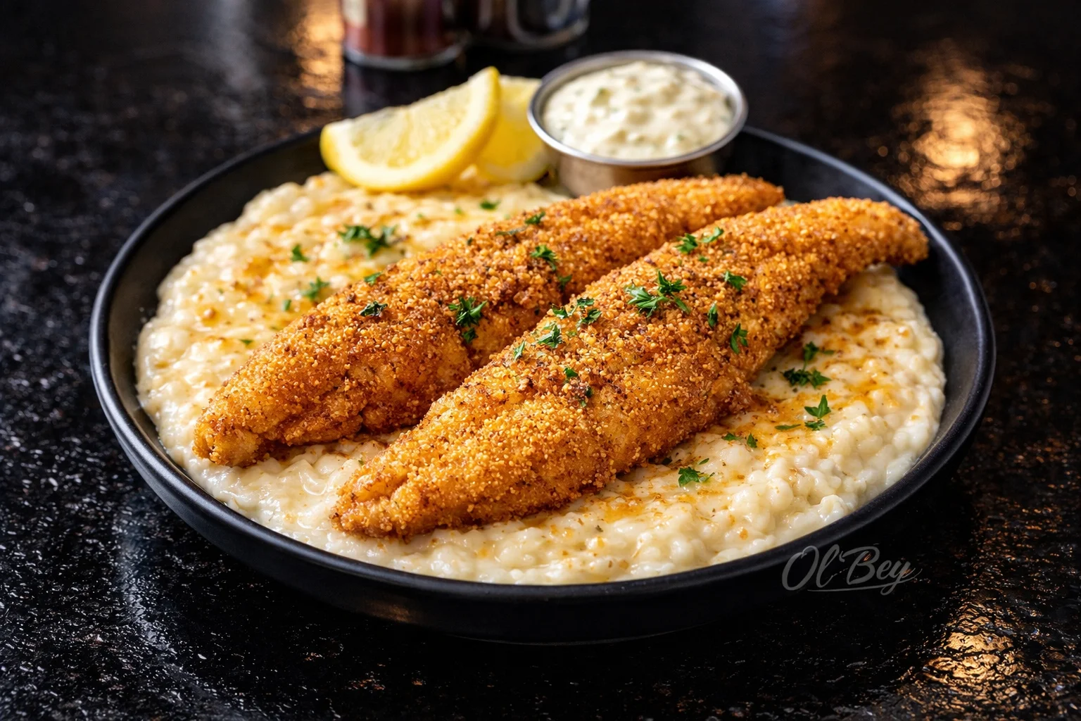 Two golden-brown fried fish fillets served over creamy grits, garnished with parsley, and accompanied by lemon slices and dipping sauce.