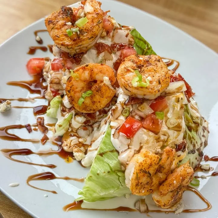 A delicious shrimp salad on a plate, featuring layers of lettuce, tomatoes, bacon, and a drizzle of sauce.
