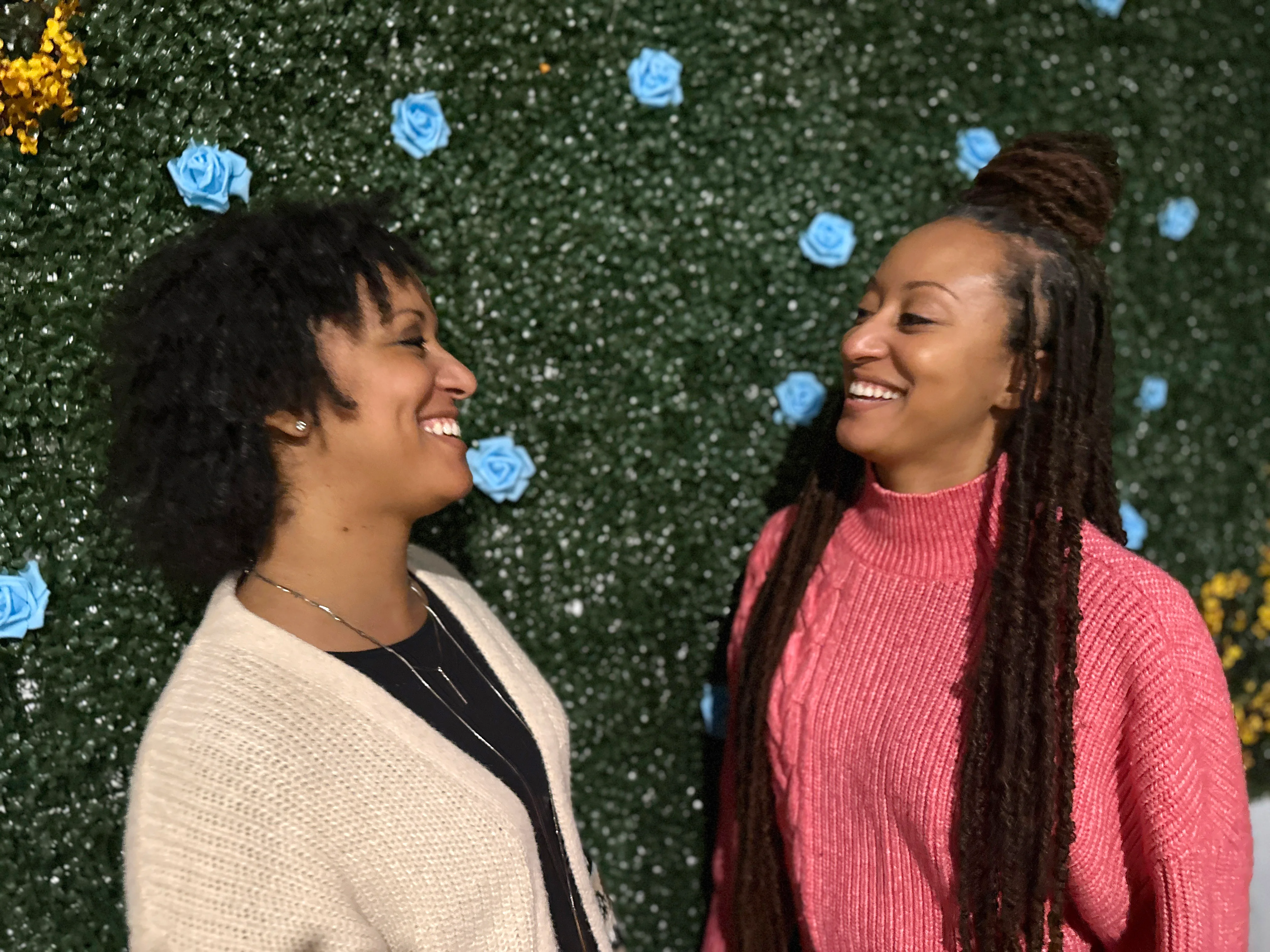Two friends smiling in front of a floral wall backdrop