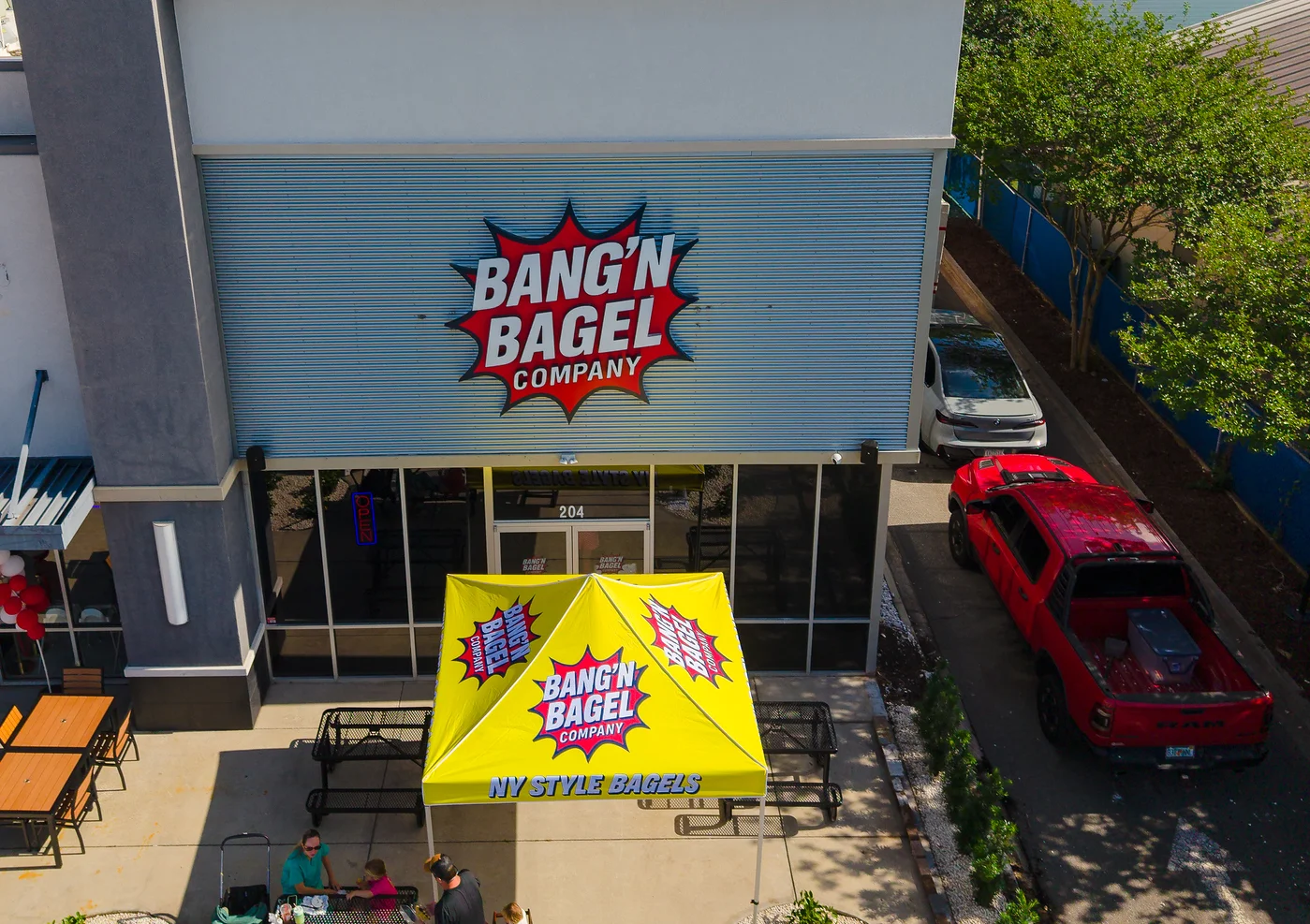 Exterior view of Bang'n Bagel Company with outdoor seating and colorful tent.