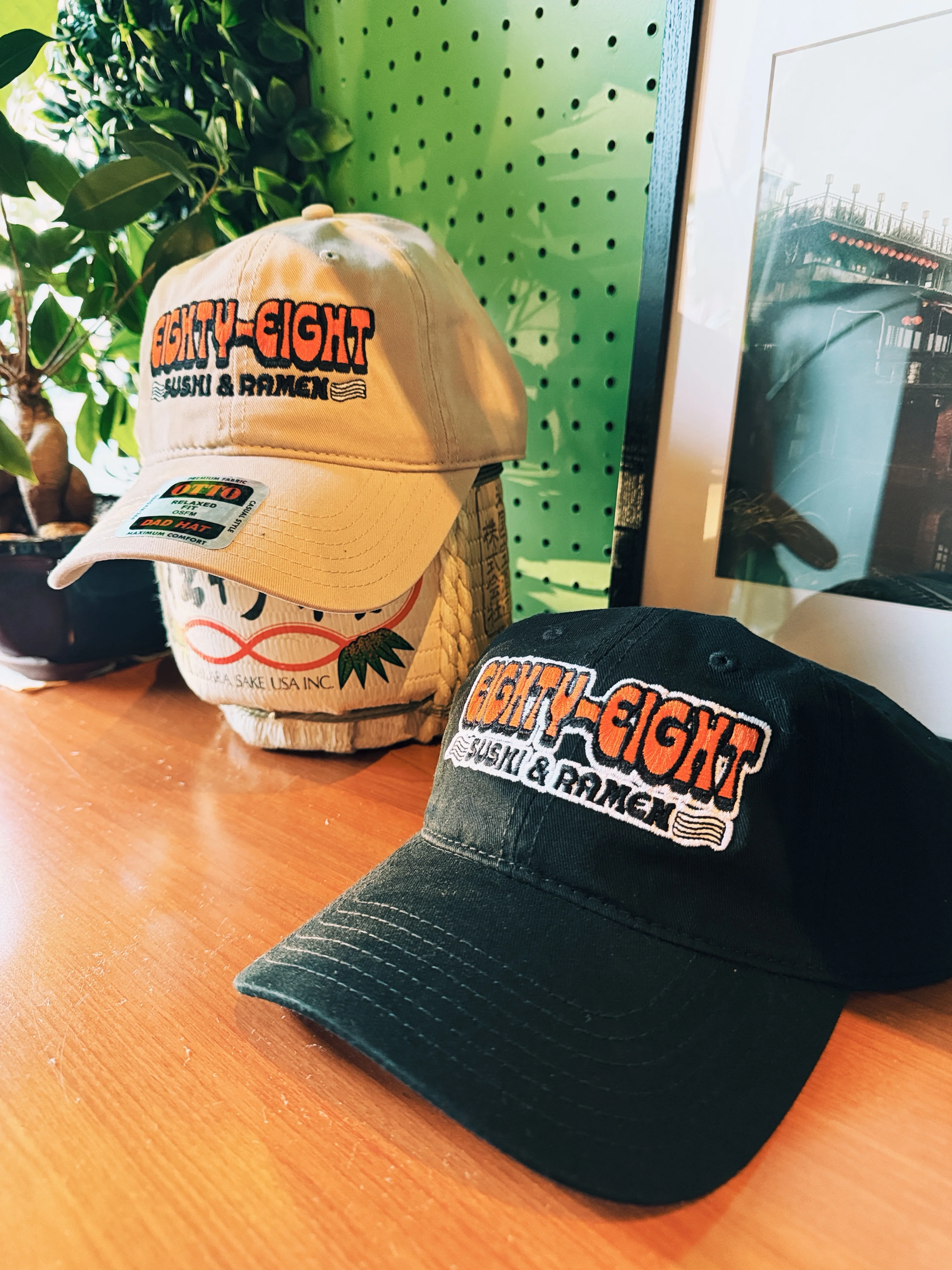 Two baseball caps displaying a restaurant logo, surrounded by decorative greenery.