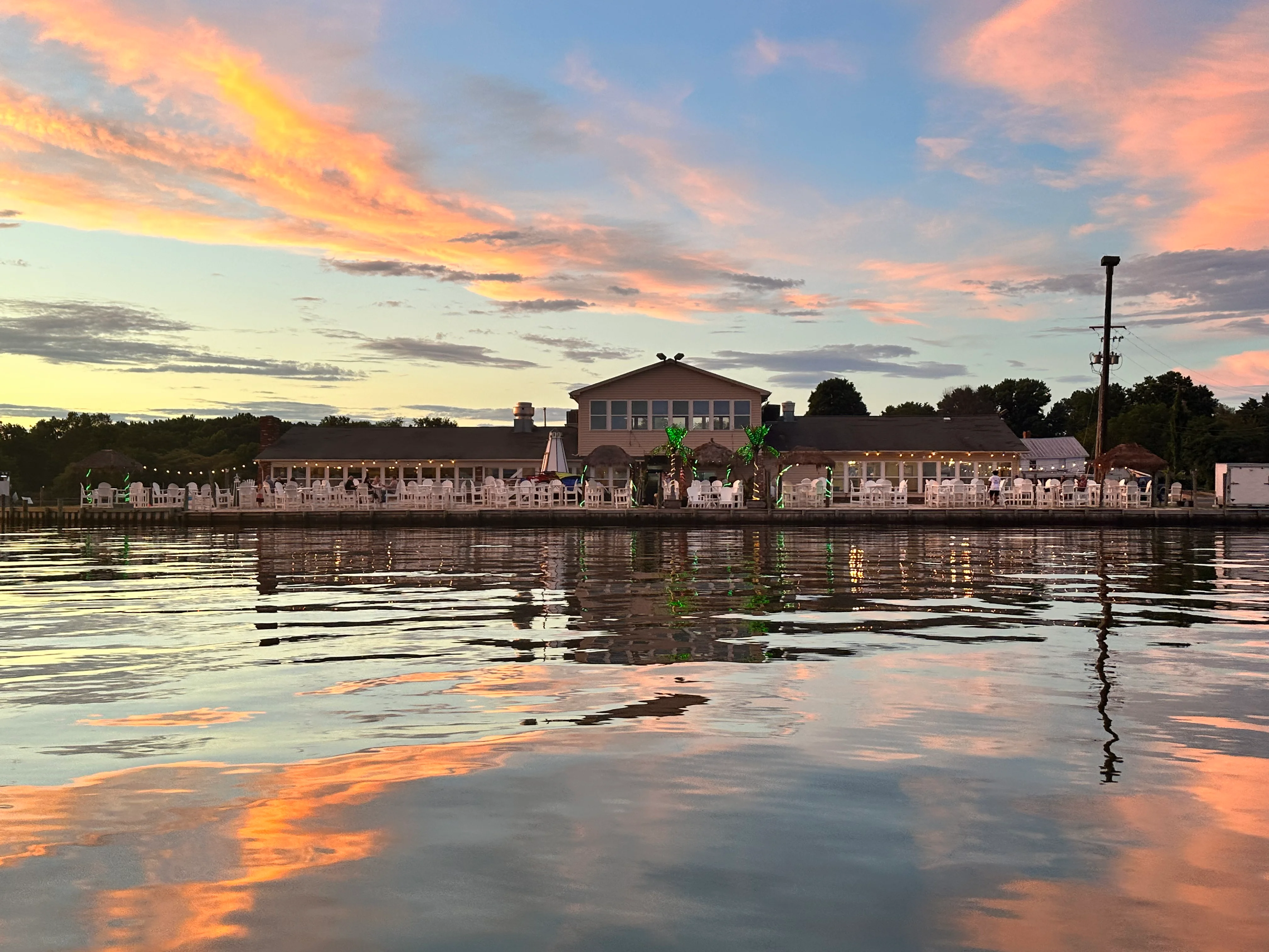 Restaurant by the water at sunset with reflections and outdoor seating.