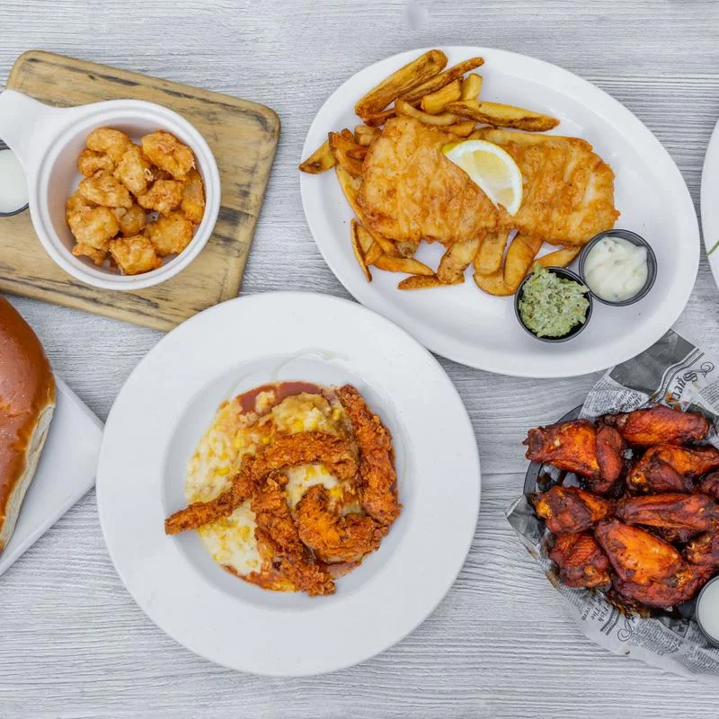 An assortment of dishes served on plates, featuring fried fish, chicken tenders, french fries, and shrimp.