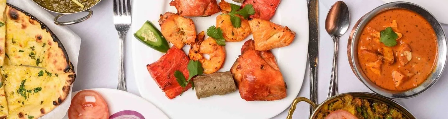 Indian food platter with red tandoori chicken, shrimp, seekh kebab, and garlic naan bread.