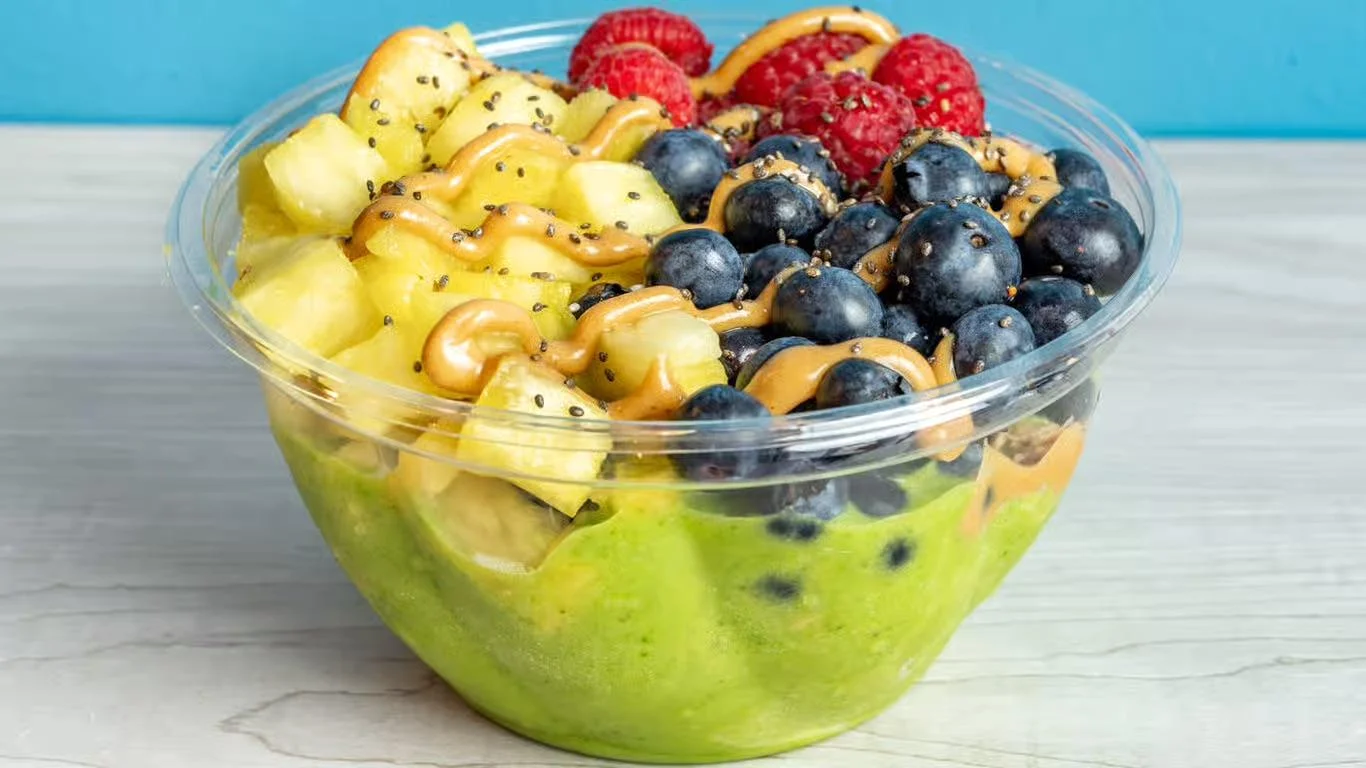 A bowl filled with a mix of fruits including pineapple, blueberries, and raspberries, drizzled with a nut butter.