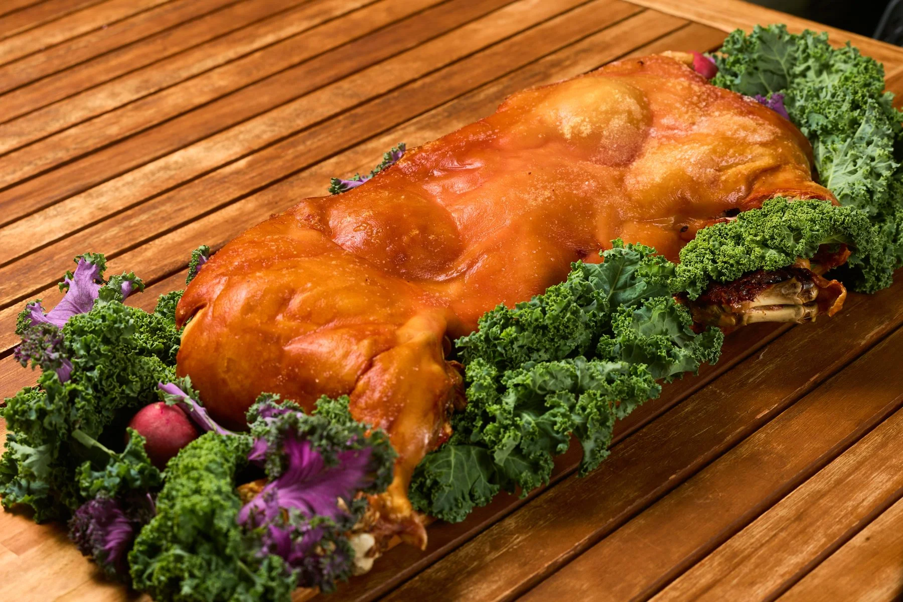 Whole roasted piglet on kale on a wooden table